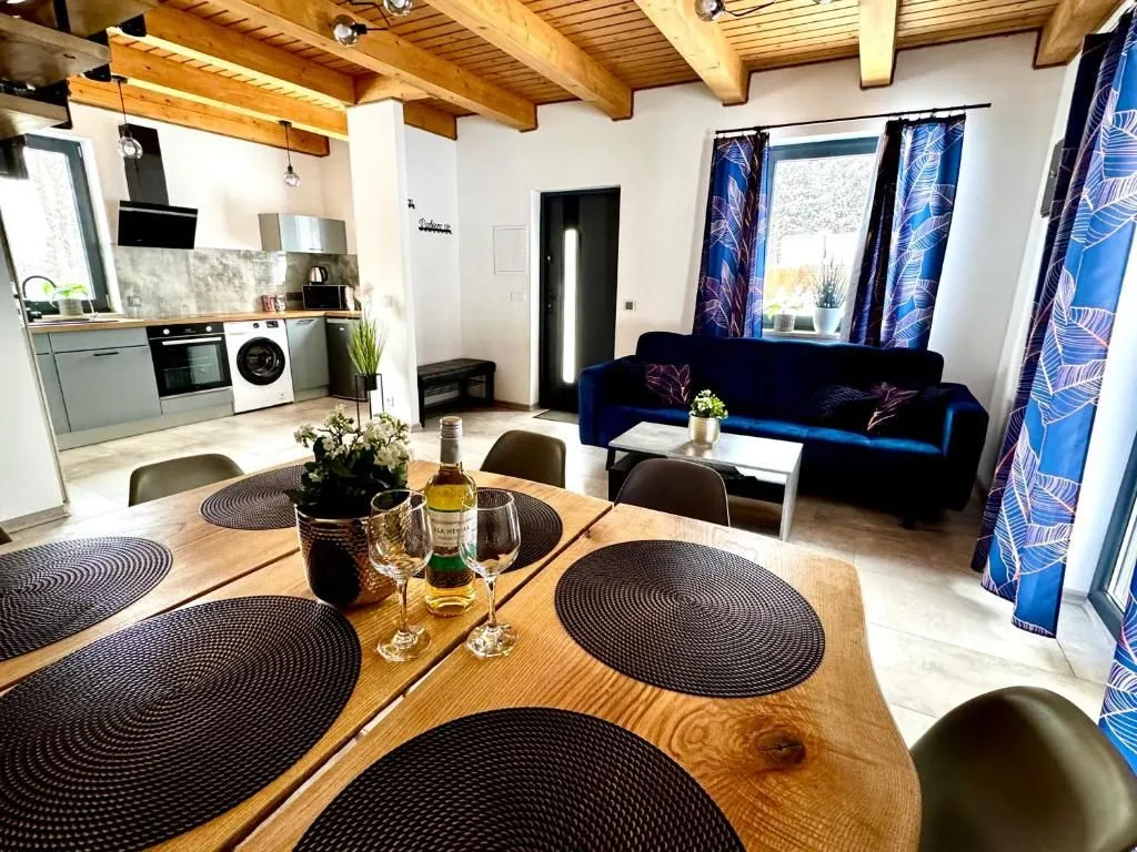 Drewniany stół w jadalni przygotowany do posiłku, w tle kuchnia i salon z sofą